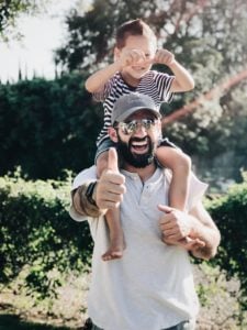 Child on shoulders of man, giving thumbs up